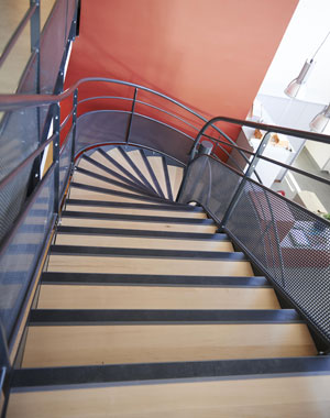 Escalier balancé avec marches en bois, garde-corps en acier laqué avec une main courante, un lisse intermédiaire et partie basse en tôle perforée. Centre social  Lyon Croix-rousse